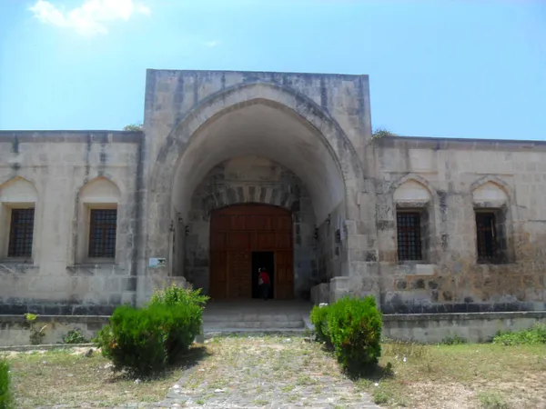 Taş duvarlarla inşa edilmiş büyük bir kervansaray yapısı, açık mavi gökyüzü ile çevrili.