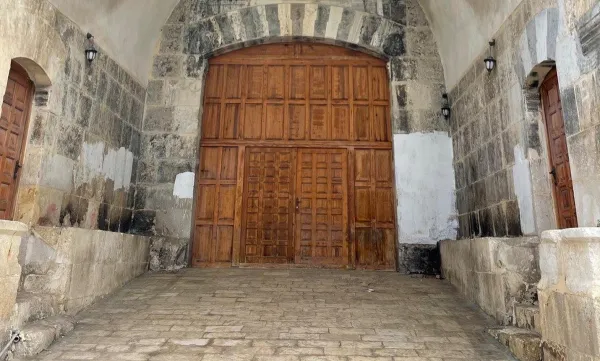 Taş duvarlarla çevrili tarihi mekan, büyük ahşap kapılar ve antik lambalar içeriyor.