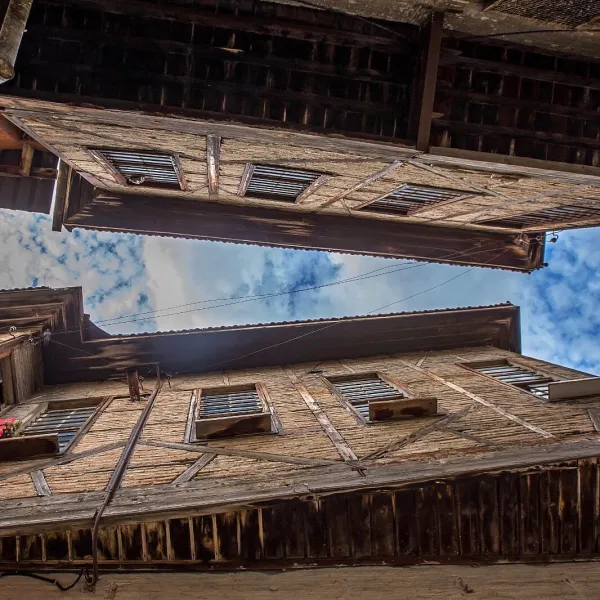 Dar sokakta yüksek ahşap binalar arasında boşluk ve mavi-beyaz bulutlu gökyüzü görünümü.