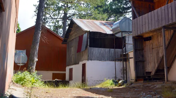 İki katlı ahşap bina ve çevresindeki doğal alanın görüntüsü.