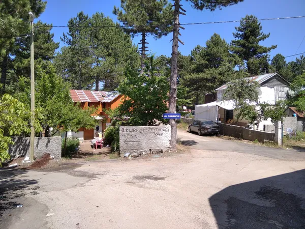 Yeşil ağaçlarla çevrili doğal bir alanda, turuncu ve beyaz yapılar görünmekte.