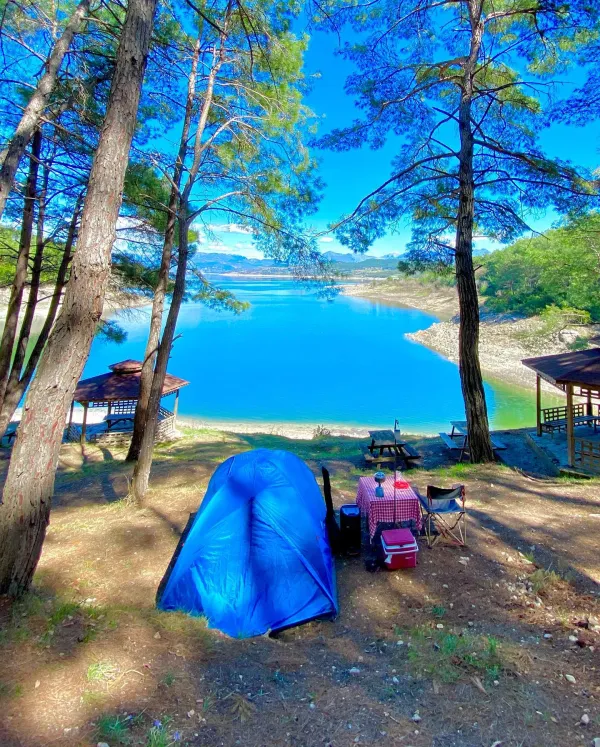 Göl kenarında mavi tente, masa ve sandalye ile kamp alanı manzarası