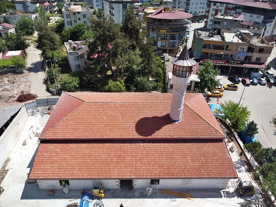 Ağcabey Camii: Osmaniye'de Tarih ve Modernizmin Sıra Dışı Buluşması! Kırmızı kiremit çatılı Ağcabey Camii, ince minaresi ve çevresindeki ağaçlar ile işçi ekipmanlarıyla görüntüle
