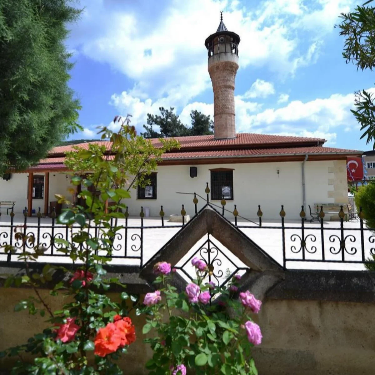Ağcabey Cami'nin Büyüsü: Tarihin İzleriyle Dolu Bir Keşif Rotası! Tarihi Ağcabey Camii, silindirik minaresi ve çevresindeki renkli çiçeklerle dikkat çekiyor.
