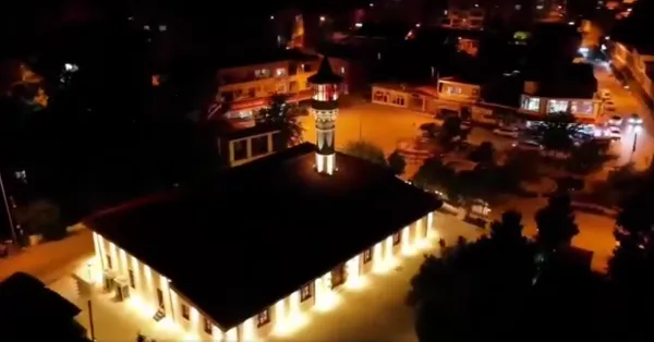 Gece vakti aydınlatılmış Ağcabey Camii, yüksek minaresi ve çevresindeki yapılarla huzurlu bir manzara sunuyor.