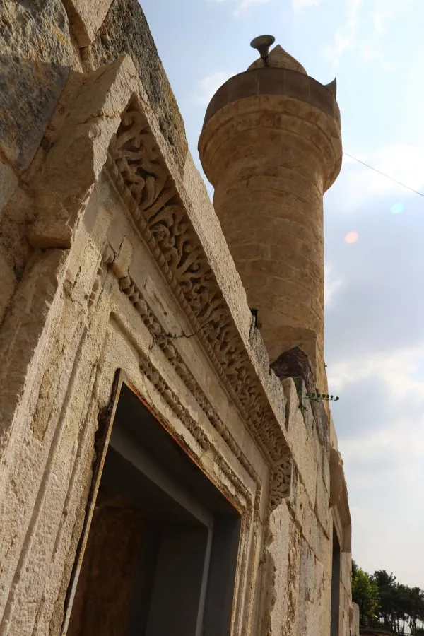Taşlardan inşa edilmiş tarihi Ala Camii, mavi gökyüzü ve ağaçlarla çevrili