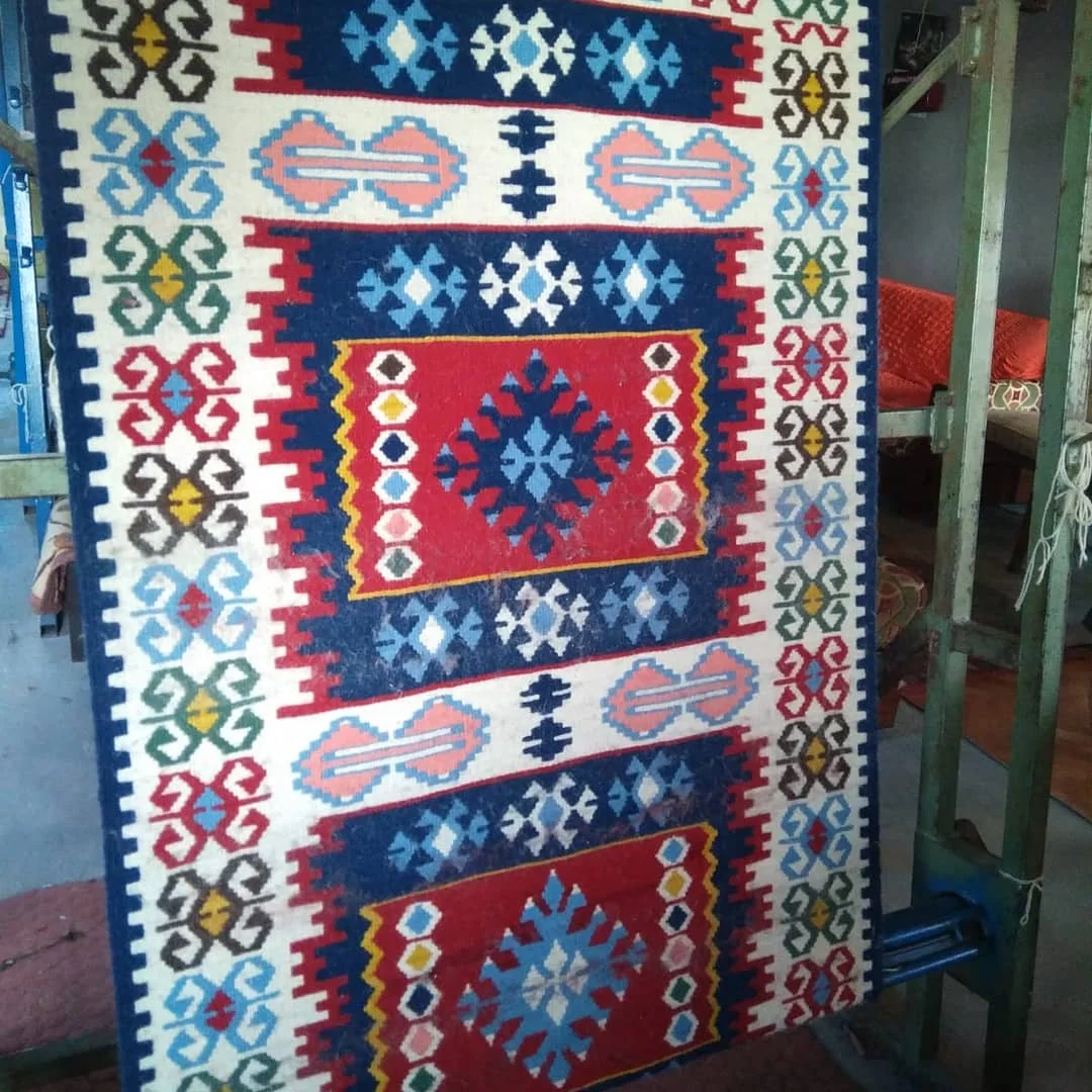 Renkli Halı Dokuma! Geometrik desenler - Karatepe Kilim Kooperatifi Canlı renklerde geometrik desenlere sahip geleneksel bir halı dokuma tezgahında sergileniyor.