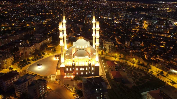 Gece vakti aydınlatılmış Abdülhamithan Camisi'nin minareleri ve kubbesi, modern binalar arasında parlıyor.