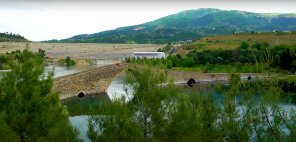 Yeşil dağlarla çevrili göletin üzerinde taş köprü ve sakin su