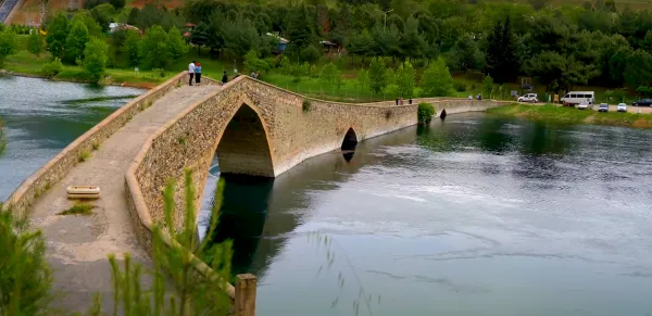 Ceyhan Köprüsü, yeşil ağaçlarla çevrili, kemerli yapısıyla nehir üzerinden geçiyor.