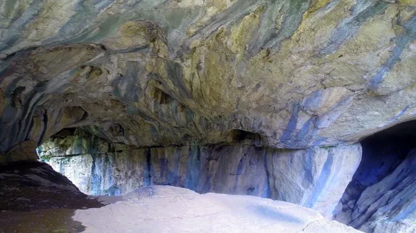 Geniş bir mağaranın iç kısmında mavi ve yeşil mineral oluşumları ile dalgalı duvarlar görülüyor.