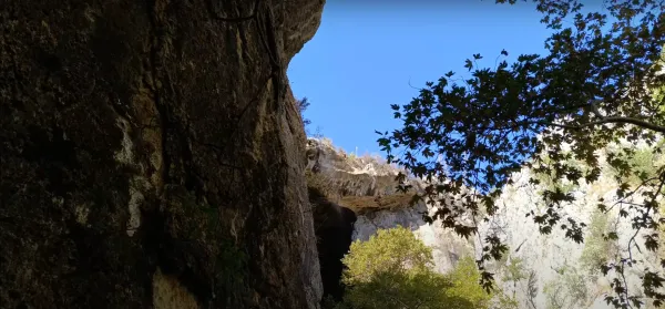 Yüksek kayalıklar arasında yeşil ağaç dalları ve açık mavi gökyüzü ile döngel mağarası