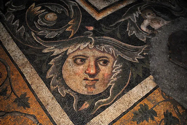 Antik mozaikte gülümseyen yüz ve bitki motifleri yer almakta.