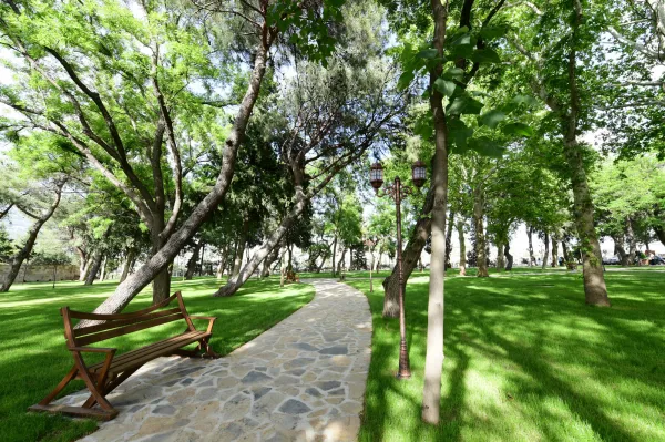 Geniş çim alanı, taş döşeli yürüyüş yolu ve ağaçlarla dolu huzurlu park