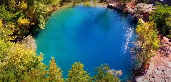 Berrak mavi suya sahip yeşil ağaçlarla çevrili gölet görüntüsü