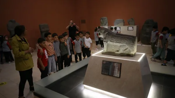 Taş bir aslan heykelinin etrafında toplanan çocuklar ve bilgilendirme panoları