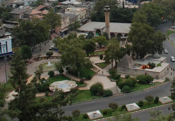 Yeşil ağaçlarla çevrili parkta minaresi ve taş yapısı olan cami görüntüsü.