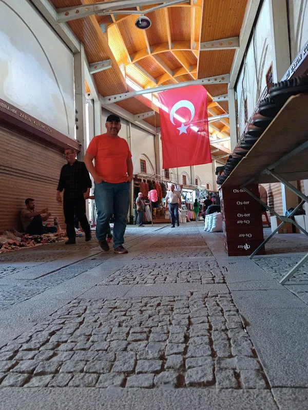 Kapalı çarşıda yürüyen insanlar, açık renkli duvarlar ve Türk bayrağı ile taş döşeme zemin.