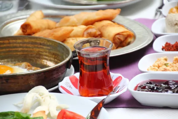 Zengin kahvaltı köşesinde bakır tavada yumurta, çeşitli mezeler ve çay yer alıyor.