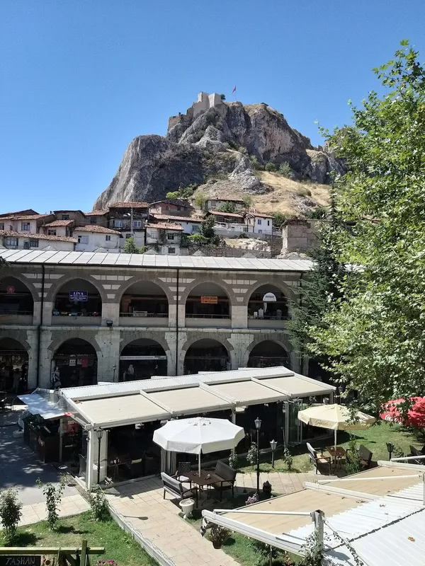 Dağın zirvesinde kale, avluda oturma alanları, açık mavi gökyüzü.