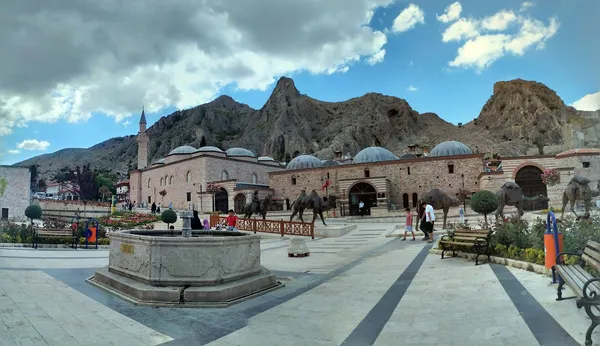 Tarihi taş hanın önünde çeşme ve çevresinde yeşil bitkilerle düzenlenmiş peyzaj.