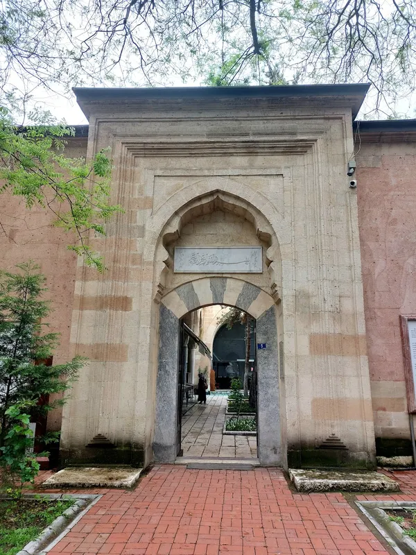 Kemerli büyük kapı, ağaçlarla çevrili bahçe ve yeşil bitkiler.