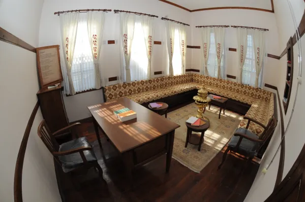 Aydınlık iç mekan, beyaz duvarlar ve geleneksel desenli kanepe ile sıcak bir atmosfer sunuyor.