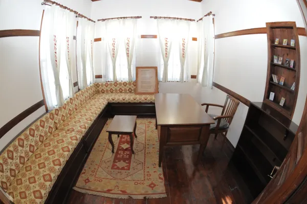 Aydınlık odada beyaz duvarlar ve ahşap çerçevelerle süslenmiş kanepe ve masa yer almakta.