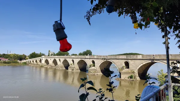 Tarihi köprü, su yansımaları ve renkli ampullerle çevrili doğal bir manzara.