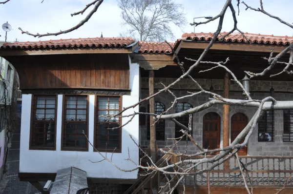 Tarihi Deligönüller Konağı'nın ahşap ve taş yapıları ön planda yer alan ağaçla birlikte görüntüleniyor.