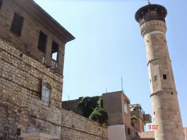 Eski taş yapı ve yüksek minare, ahşap balkon ve küçük pencerelerle dikkat çekiyor.