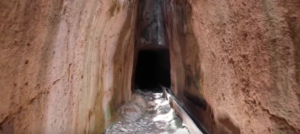 Yüksek duvarlarla çevrili dar geçit, karanlık derinlikler ve küçük taşlarla dolu zemin.