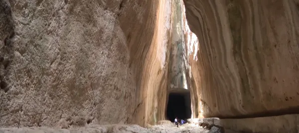 Büyük bir kanyon içerisinde yürüyüş yapan insanlar ve karanlık bir mağara girişi