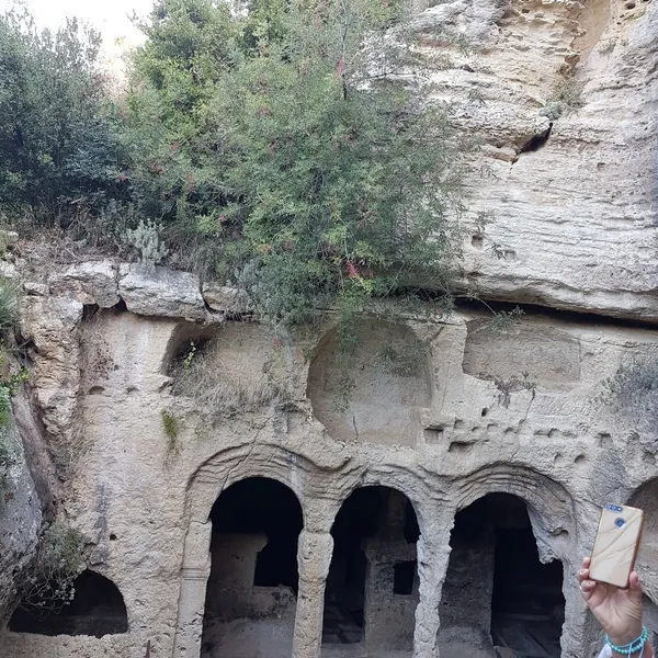Doğal kaya oluşumunda tarihi yapılar ve yeşil bitkilerle dolu bir alan, cep telefonu ile görüntü kaydediliyor.