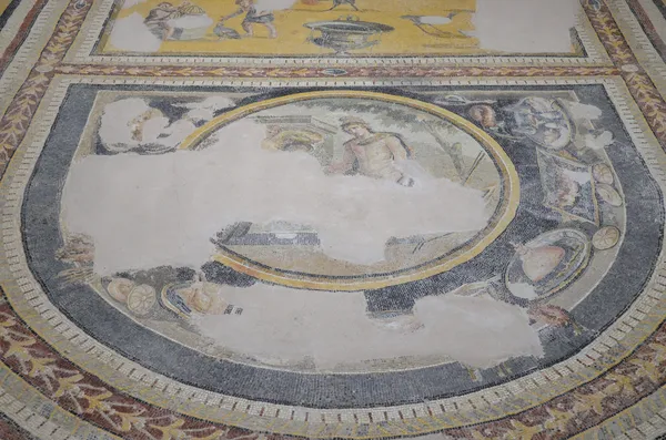 Merkezde dairesel tasarım ve etrafında figürler bulunan antik mozaik