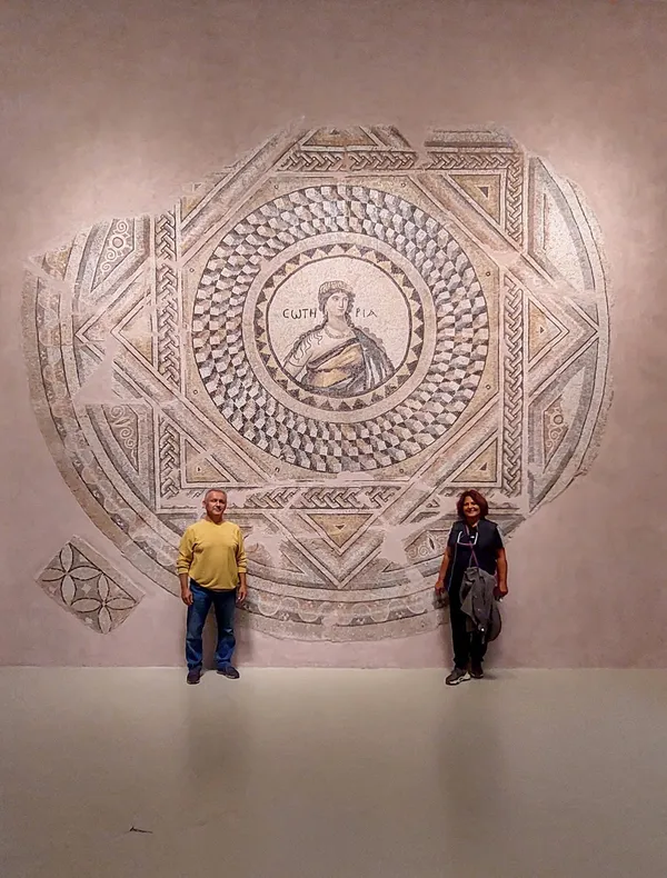 Antik mozaik eseri etrafında duran iki kişi, detayları inceliyor.