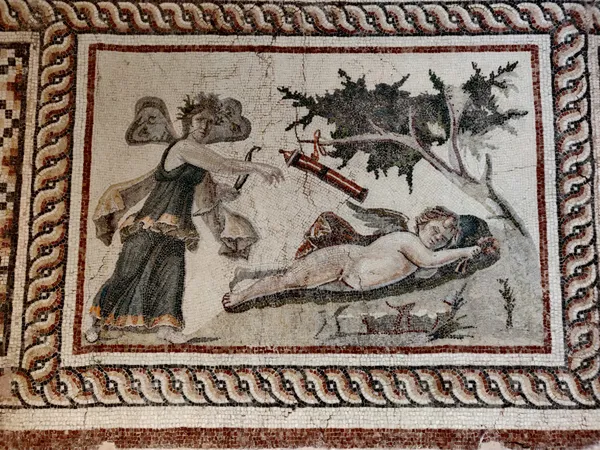 Antik mozaikte uzun elbiseli figür ve yastıkta yatan çocuk betimleniyor.