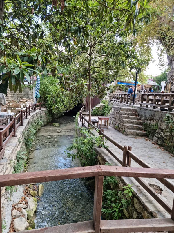 Yeşil ağaçlar arasında nazik bir dere ve yürüyüş yolları görünmekte.