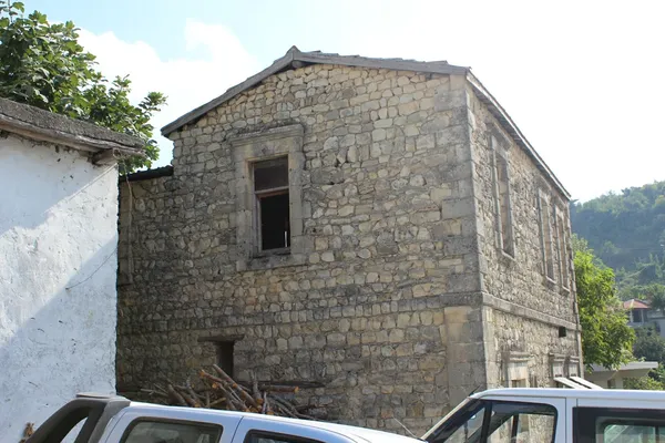 Tarihi taş duvarlı bina, ahşap pencereler ve yeşil ağaçlar ile çevrili