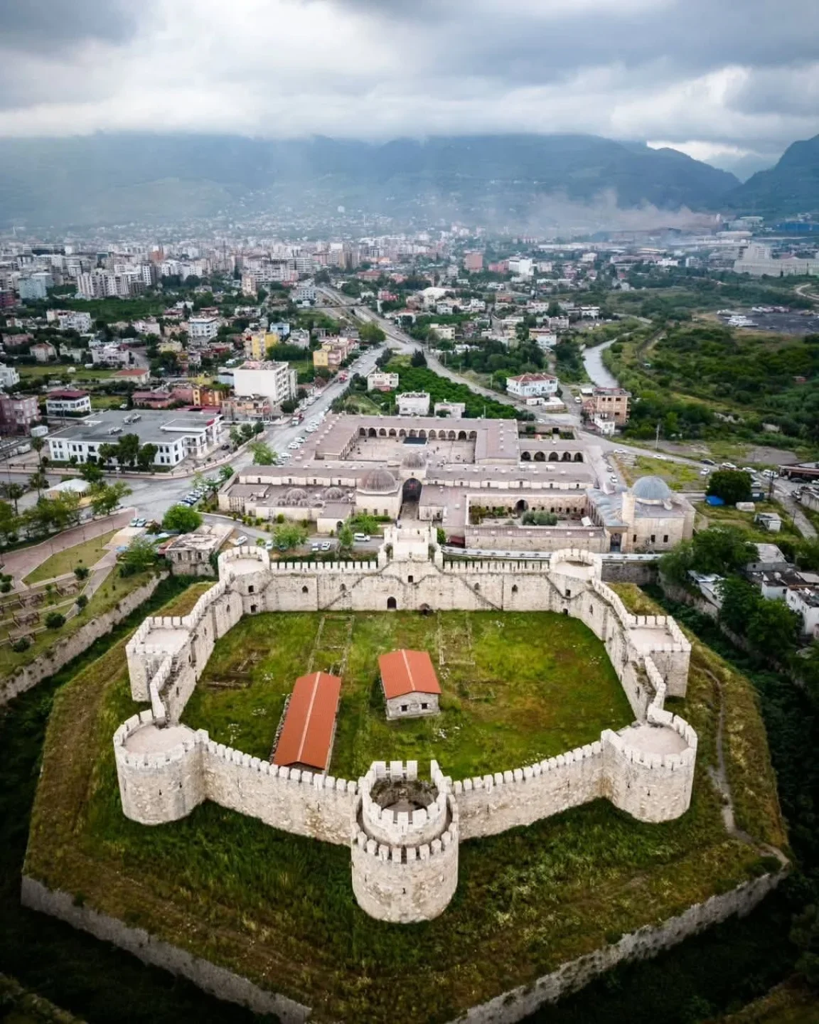 Tarihin Gölgesinde: Payas Kalesi - Modern şehir manzarasıyla iç içe! Tarihi Payas Kalesi, kalın taş duvarlar ve yeşil alan ile modern şehir manzarası arasında yer alıyor.