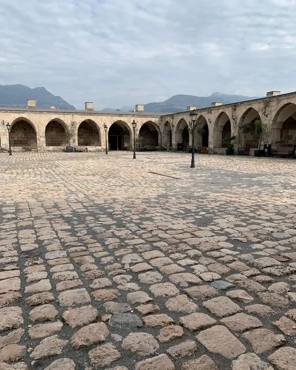 Geniş bir avluda taş döşeme ve kemerli geçitler, uzakta dağ silüeti ile birlikte.
