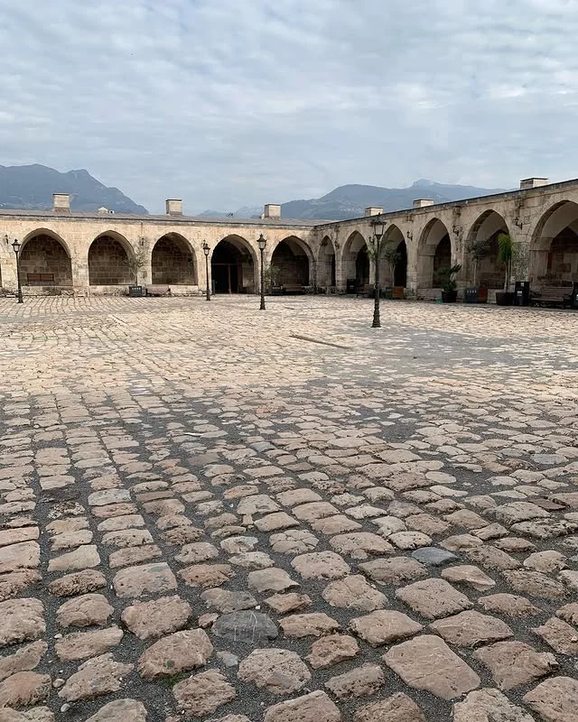 Tarihi Avlu - Taş döşeme ve kemerli geçitler, dağ silüetiyle Geniş bir avluda taş döşeme ve kemerli geçitler, uzakta dağ silüeti ile birlikte.