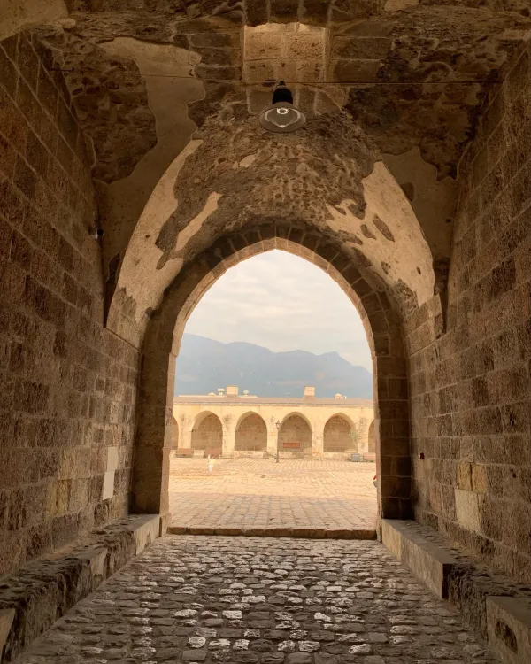 Tarihi kemerli geçidin içinden görülen dağ manzarası ve avlu