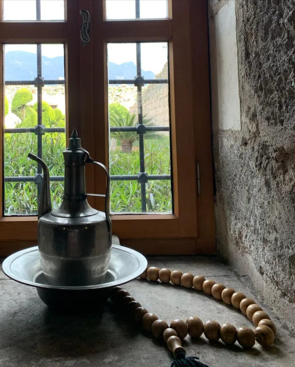 Açık pencere önünde metal sürahi, tesbih ve bahçe manzarası