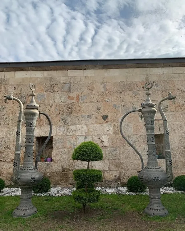 Gösterişli metal sürahiler ve taş duvar önündeki çalılar