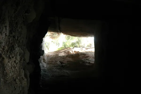 Karanlık bir mağarada doğal taş duvarlar ve ışık dolu bir açıklık.