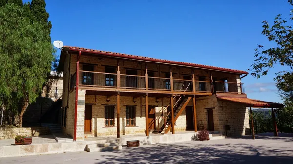 İki katlı doğal taş yapının rustik görünümü, geniş balkonlar ve çevresindeki yeşil alan.