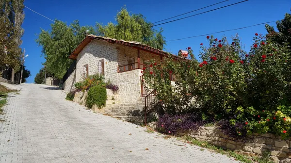 Taş duvarlardan oluşan ev, bahçede renkli çiçekler ve mavi gökyüzü ile çevrili.