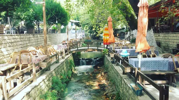 Taş duvarlarla çevrili, ağaçlarla dolu terasta yer alan restoran alanı.