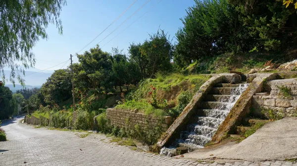 Taş döşeli yol boyunca akan küçük şelale ve çevresindeki yeşil alan